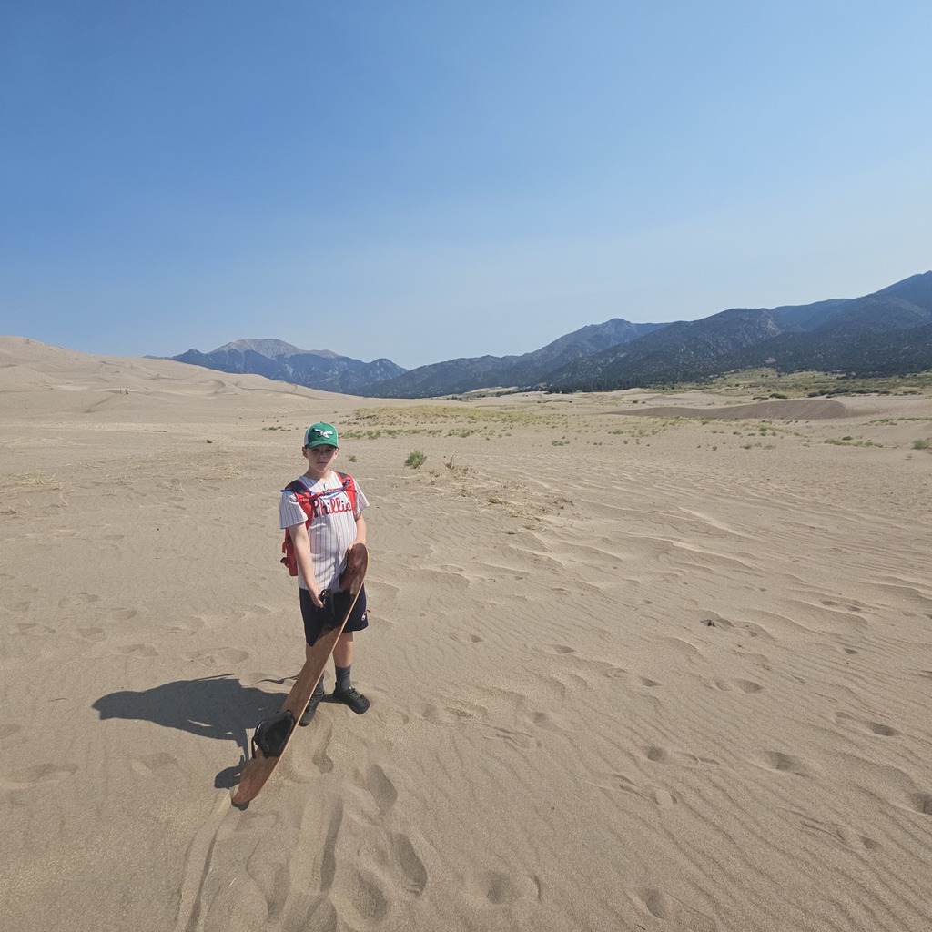 Ben holds a sand board in a desert with mountains in background