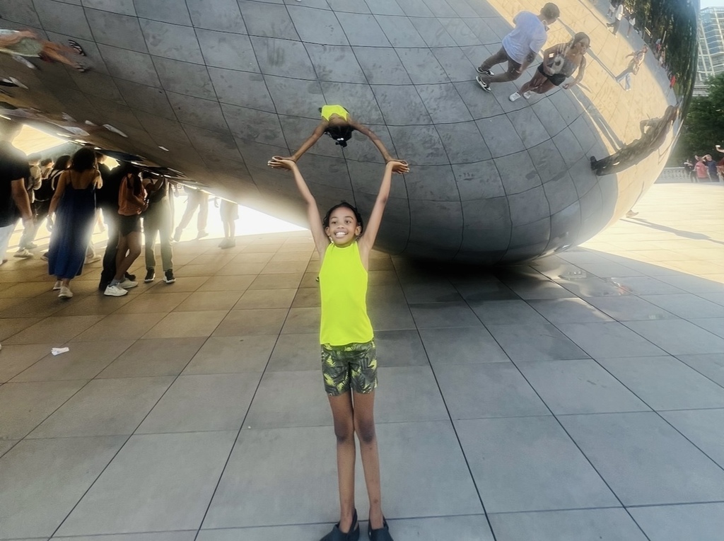 Mckesson stands beneath a shiny mirrored sculpture with her hands up, with her reflection appearing like she is supporting the huge mass