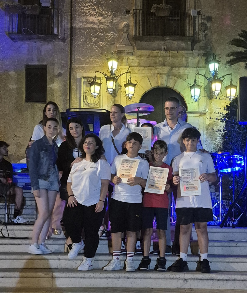 Pasquale stands on stone seps with his family, with a beautiful stone building with arches and lanterns behind them