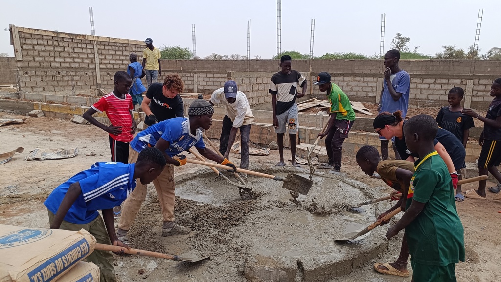 Students and members of the community work together to full a stone structure with concrete with spades and shovels