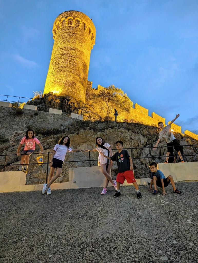 5 Abington students pose in front of a brightly lit medieval tower in Spain at dusk