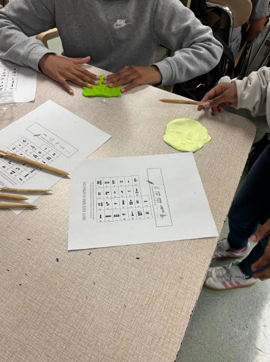 Image of 6th grade students writing their names using reeds and clay.