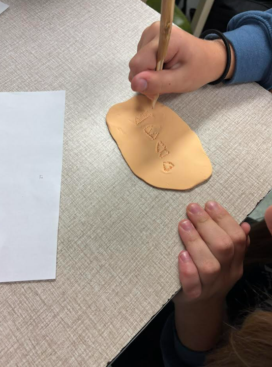 Image of 6th grade students writing their names using reeds and clay.