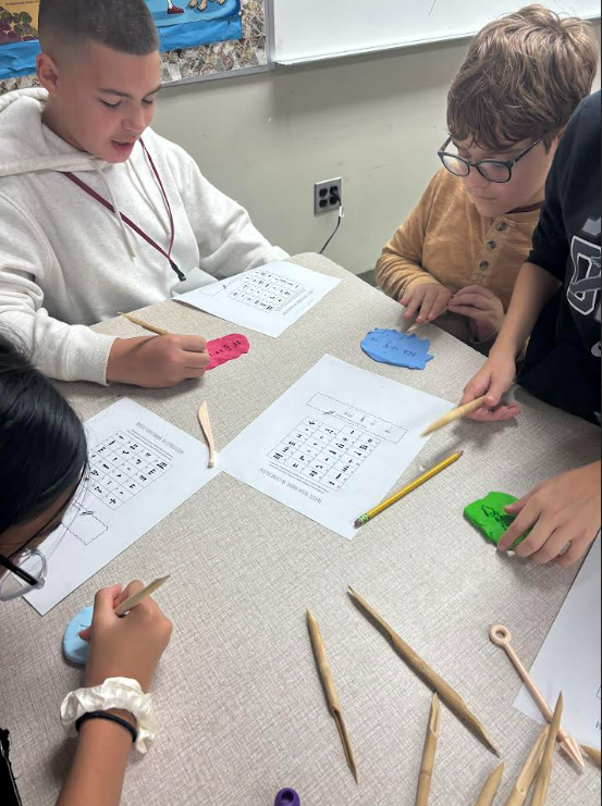 Image of 6th grade students writing their names using reeds and clay.