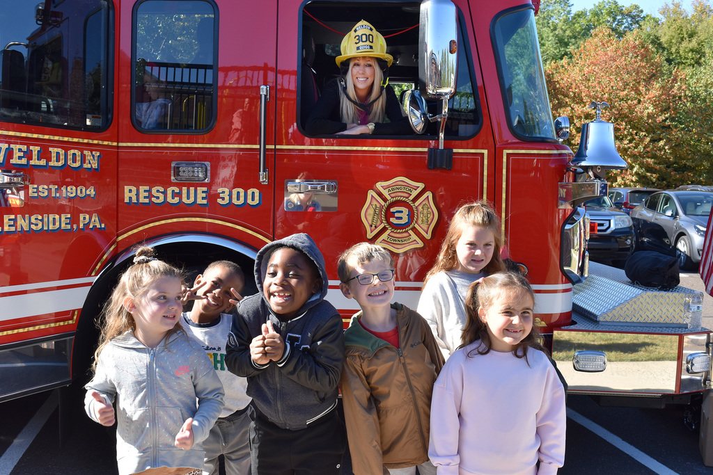 Principal Stokes wears a fireman's hat while looking out the window of the Weldon fire truck, with kindergarteners posing happily in the foreground