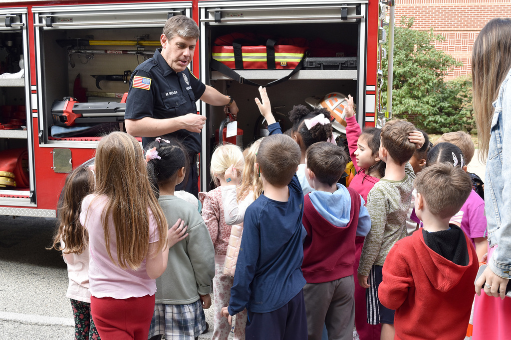 Overlook kindergarteners gather around a firefighter demonstrating what types of hoses are on their fire truck