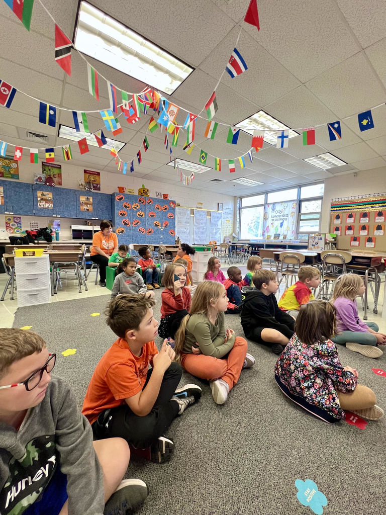 Students sit on a rug and listen to Dr. Fecher read