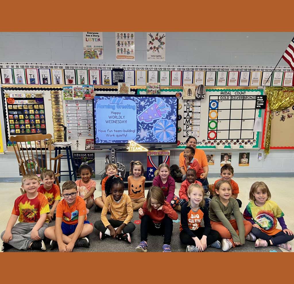 Mrs. Oldham sits and poses with her students in front of her classroom