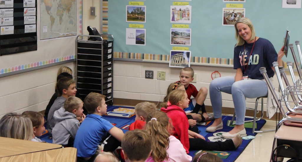 A teacher reads to students who are sitting on a carpet before her