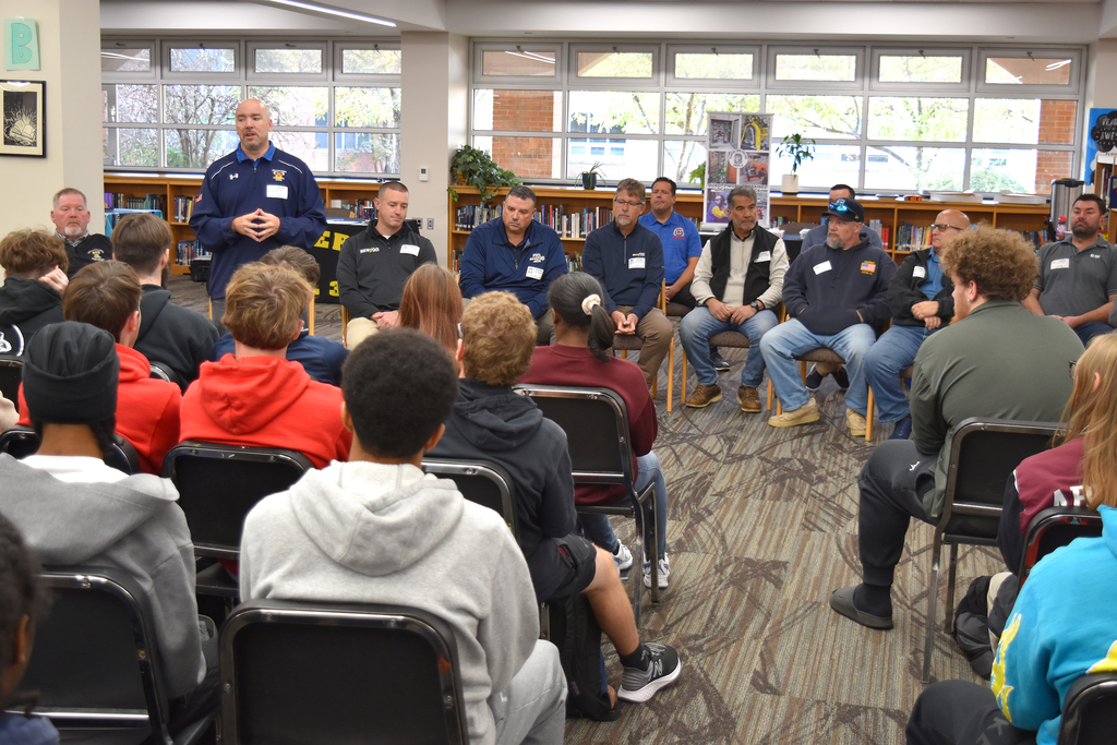 A union representative stands and speaks to ASHS students, in front of a seated row of representatives.