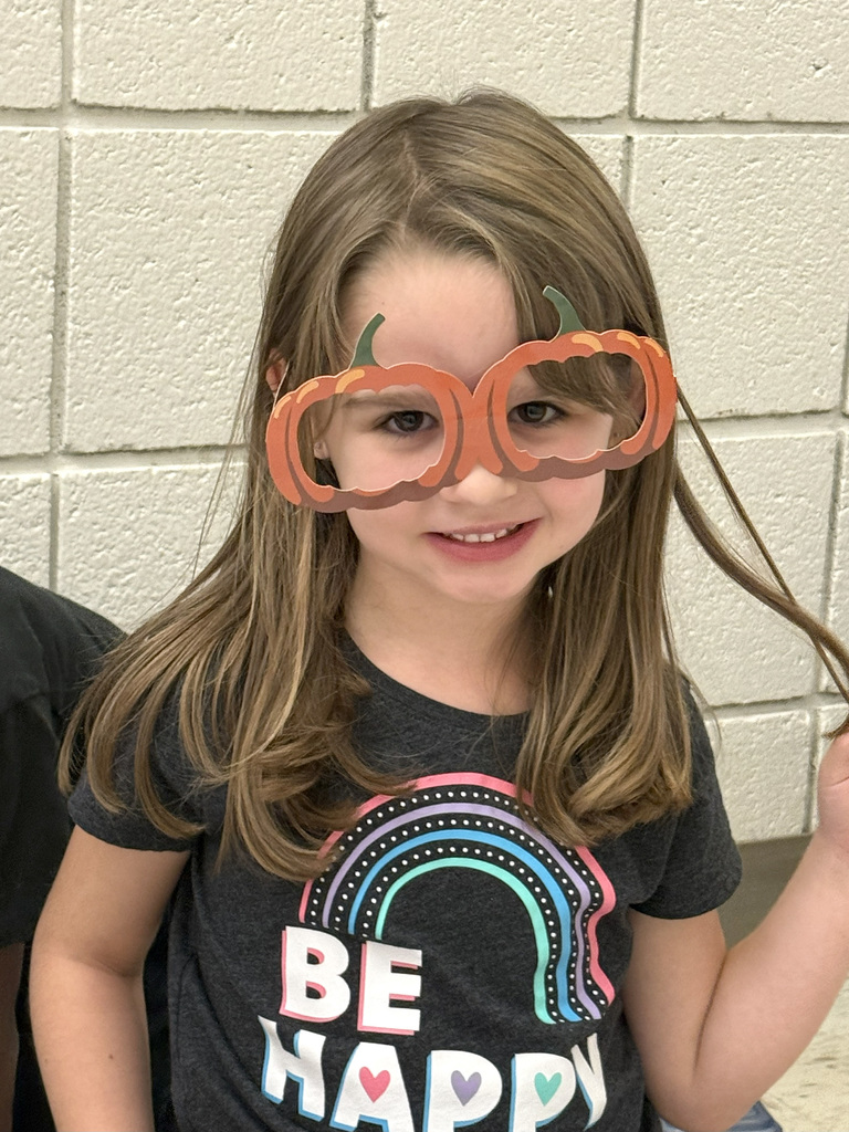 A kindergartener smiles wearing pumpkin eye glasses