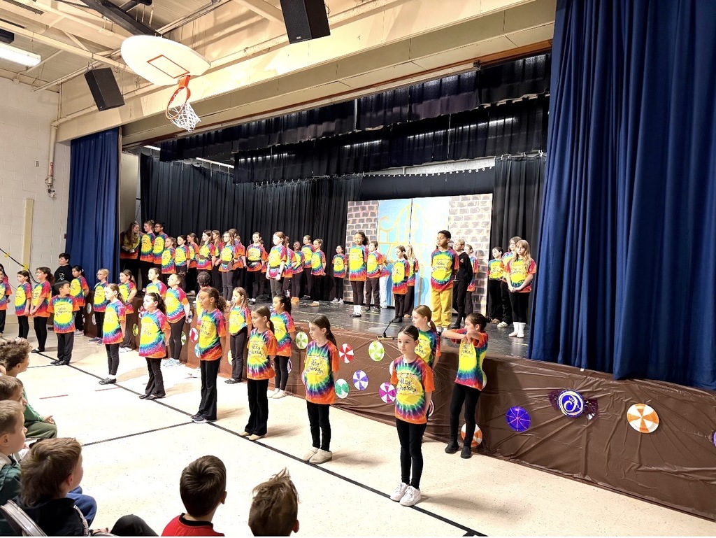 McKinley Drama Club students stand on stage in colorful t-shirts in "Willy Wonka, Jr." 