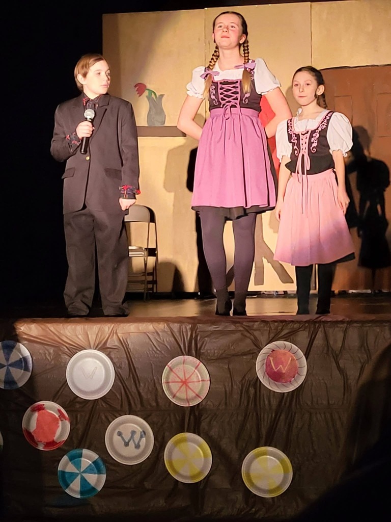 Students stand on stage in costumes performing in "Willy Wonka, Jr."