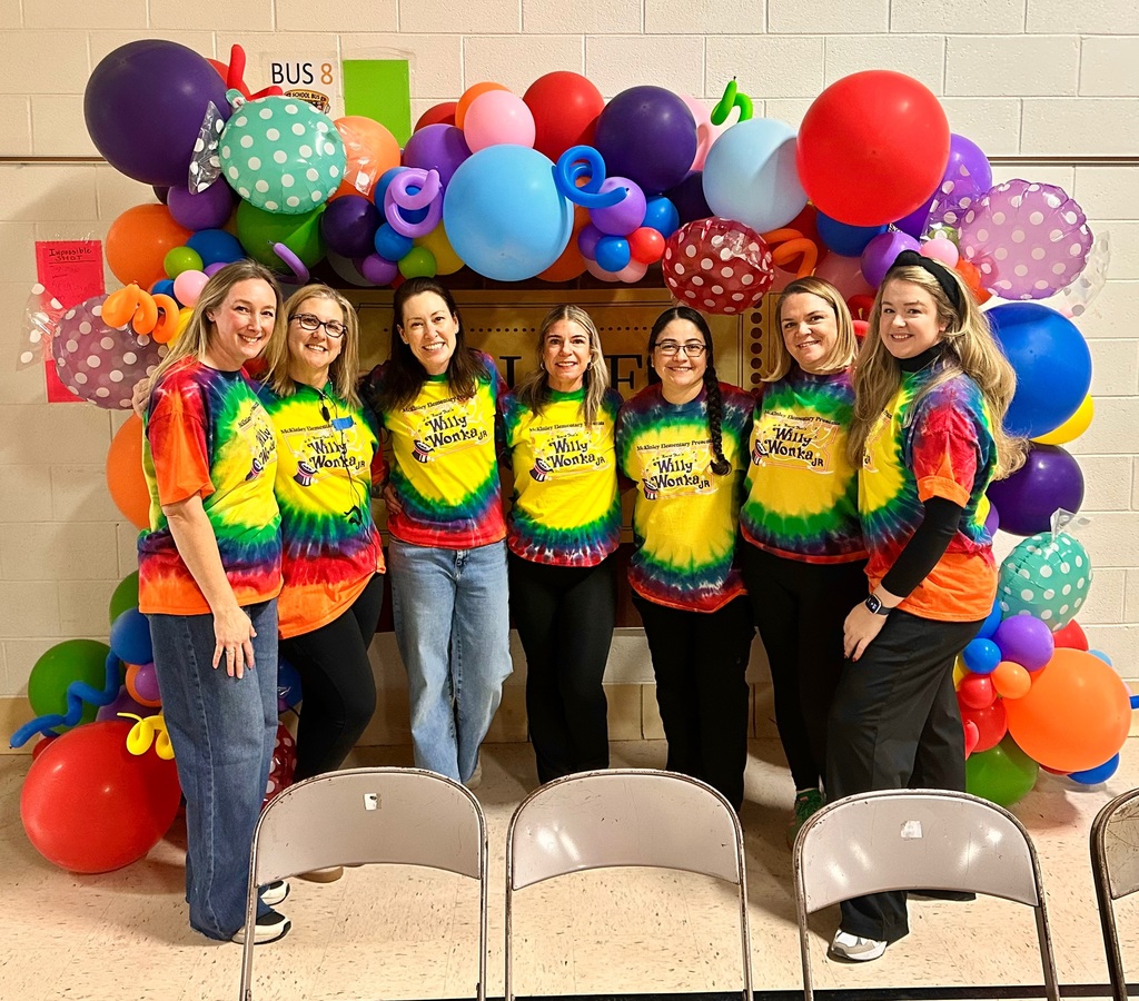 Volunteers who helped produce the play stand together under an arch of colorful balloons