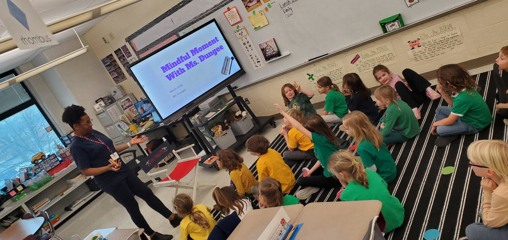 Mrs. Dungee speaking to students sitting on a carpet.