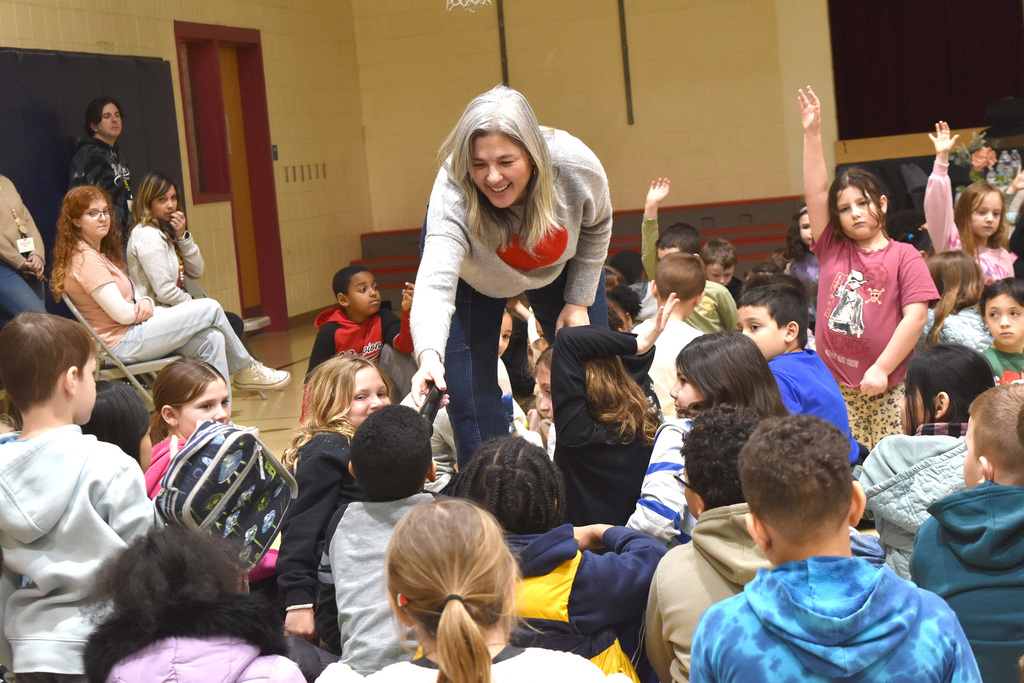 Students raise their hands to ask questions while Ms. Mei Chase holds the microphone for a student to speak