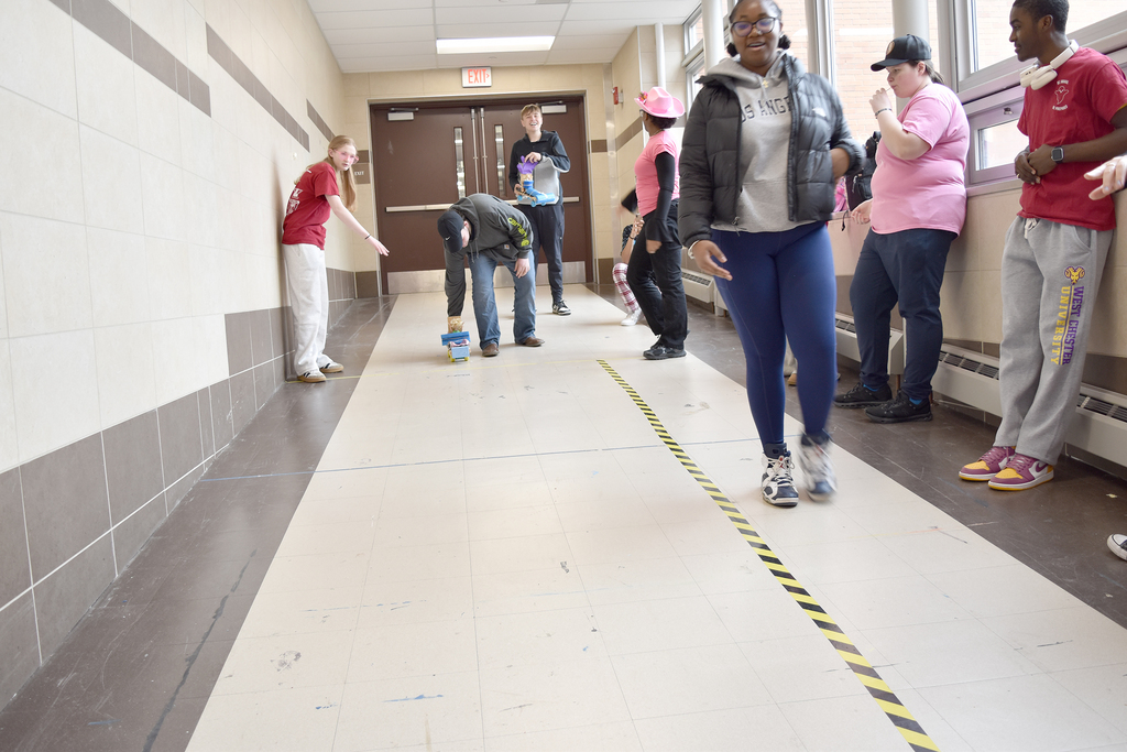 Students roll toy vehicles down an incline to learn how speed and velocity affect collisions
