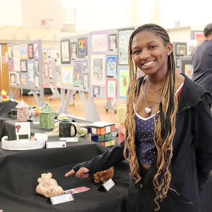 A student points proudly at her 3-D sculpture on display and smiles