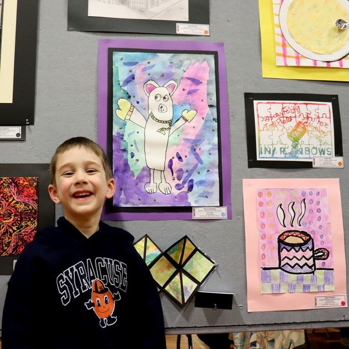 A student stands in front of his displayed artwork and smiles brightly