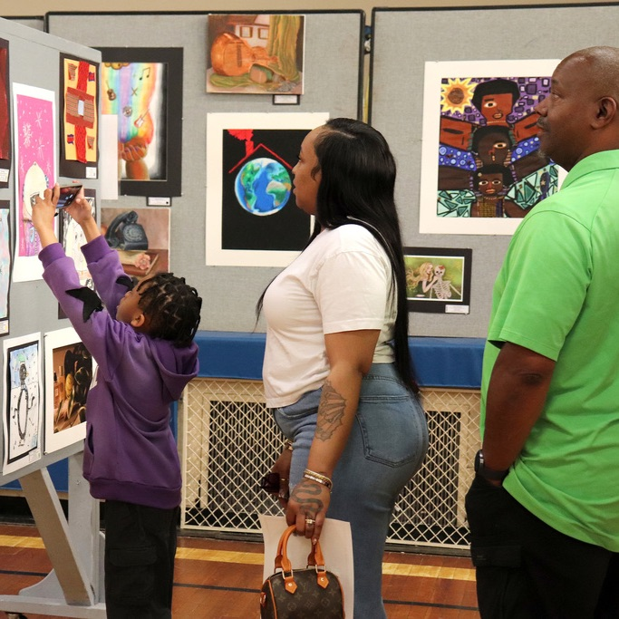 A young student takes a picture of his landscape artwork with a cell phone