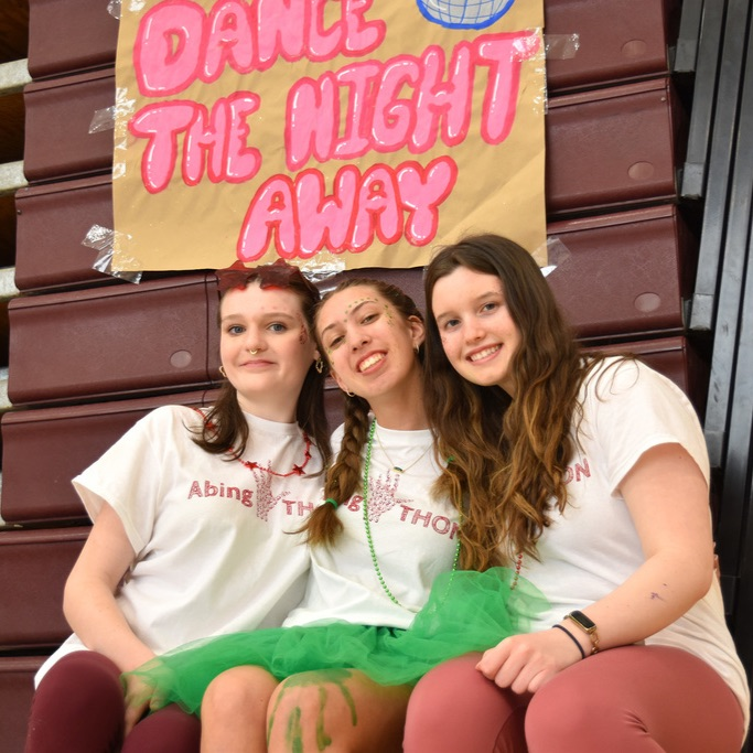 3 students pose under a sign saying "Dance the Night Away" at AbingTHON