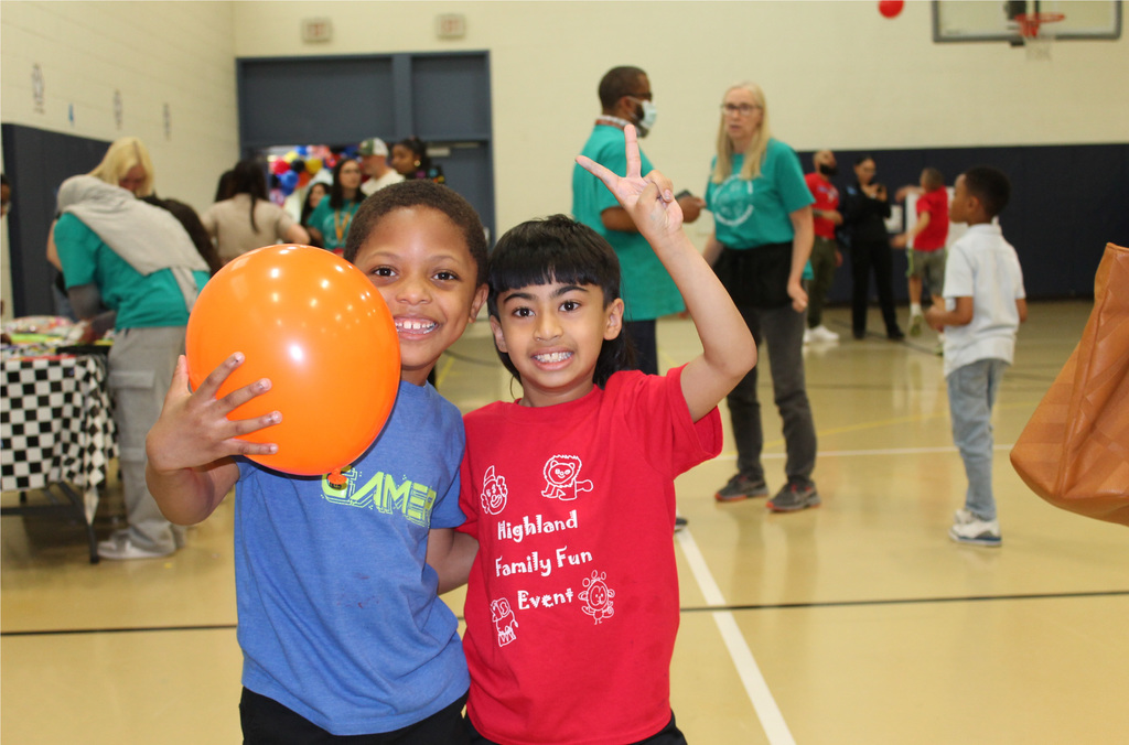 Two students smiling, holding an orange balloon at Highland's Autism Awareness event.