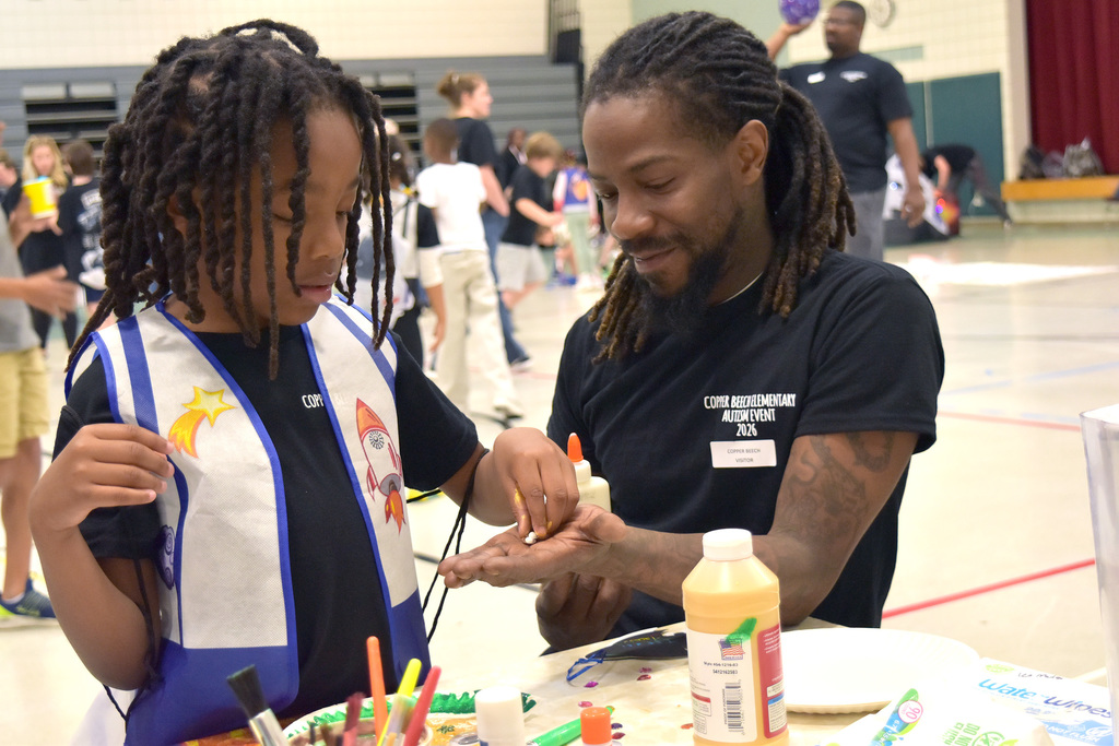 A staff member helps a student with a craft at the Copper Beech Autism Awareness event