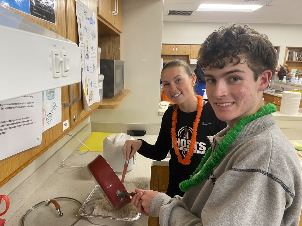 Two students transfer cooked rice from a frying pan to a container in their classroom