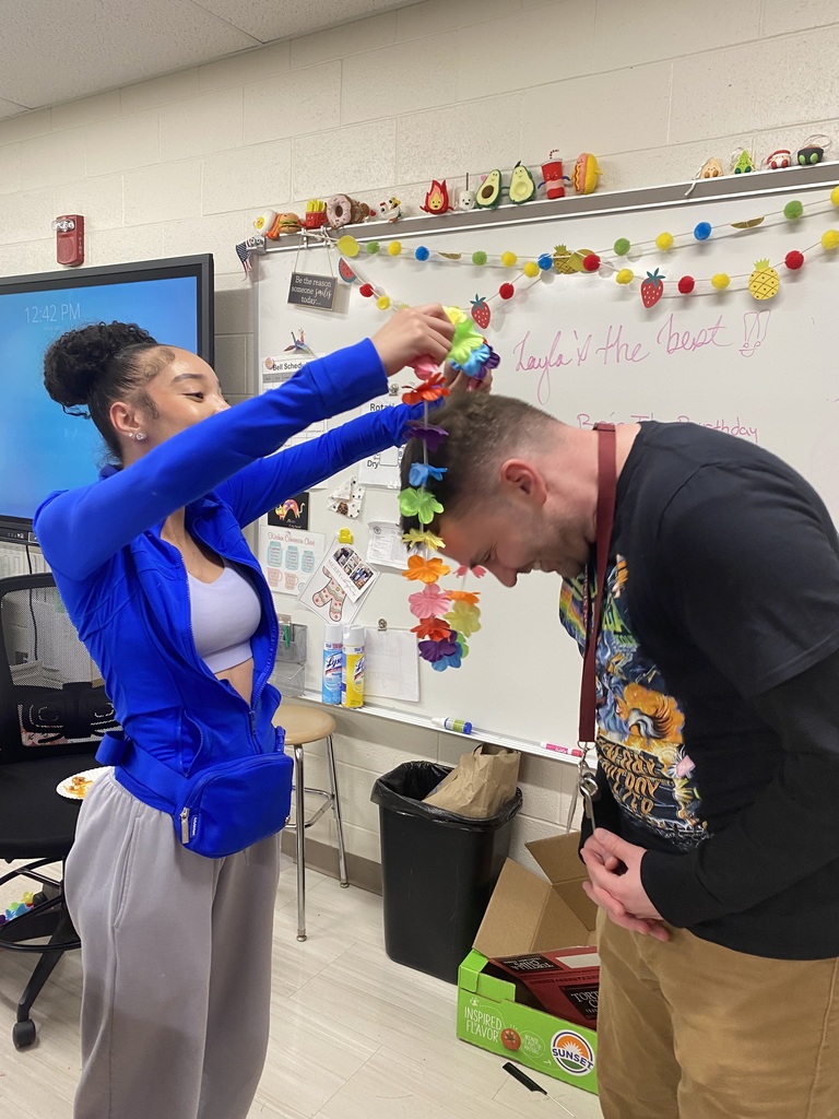 A culinary student places a colorful lei necklace around the neck of Mr. Schneider