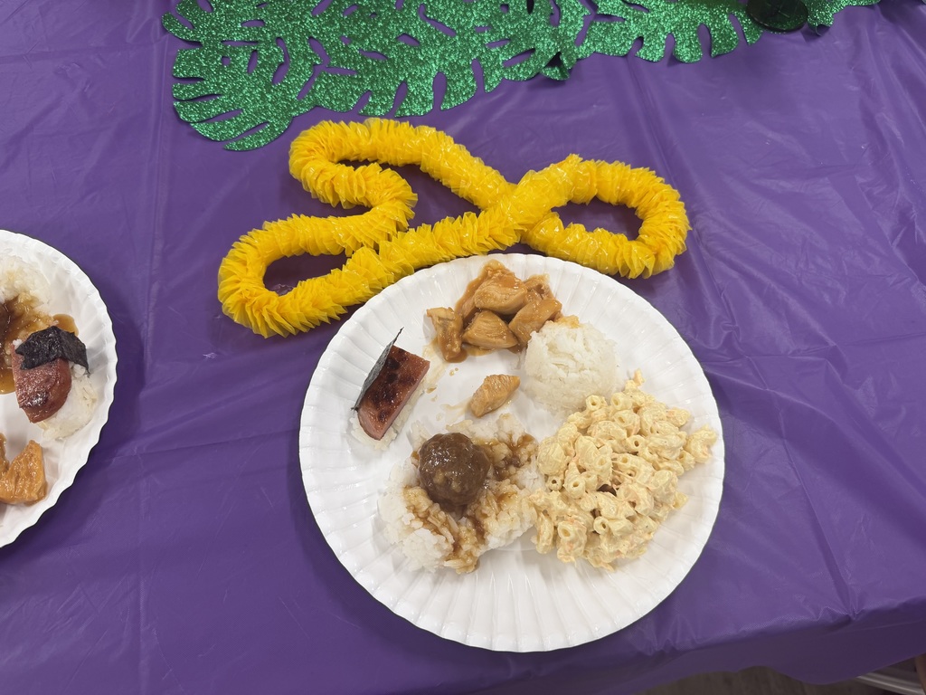 A plate of Hawaiian food on a purple tablecloth with a yellow lei necklace