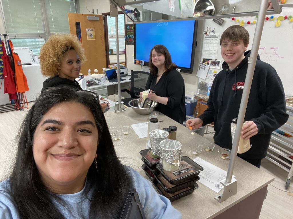 Abington High School students and teacher preparing a meal and smiling at camera