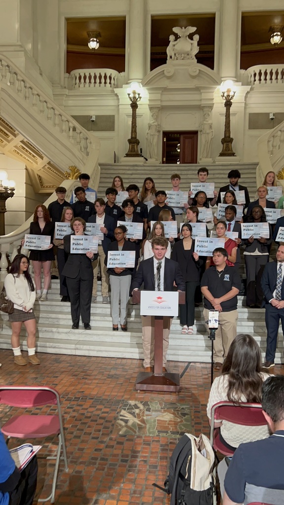 Students stand on the capitol stairs, holding signs saying "Invest in Public Education"