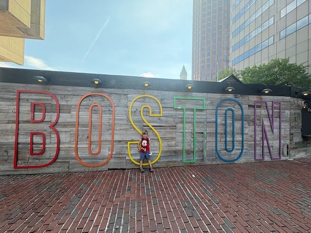 Eric stands against a wooden wall with Boston spelled in large colorful letters