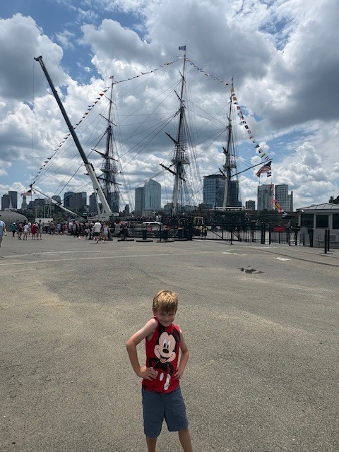 Eric poses with front of tall ships and city of Boston in background