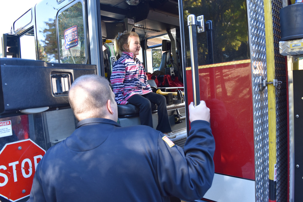 A student smiles as sits in the firetruck, assisted by a firefighter