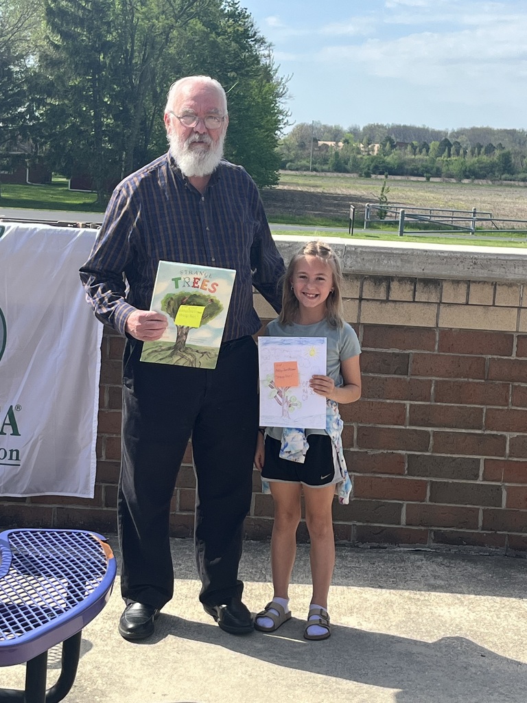 Mayor standing with student receiving book as prize outside on the patio