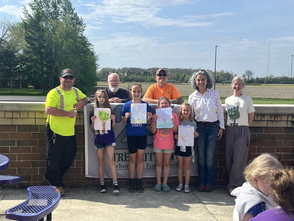 Four students standing in front of a sign with four adults behind them