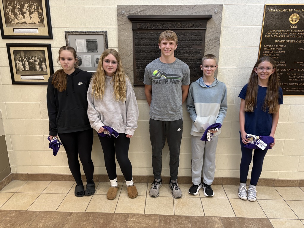 five students standing in front of wall holding t-shirts