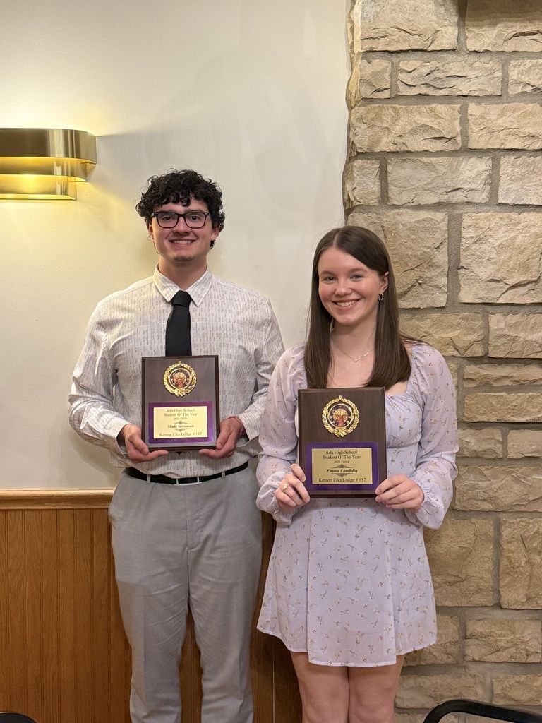 Two students holding plaques standing in front of a stone wall