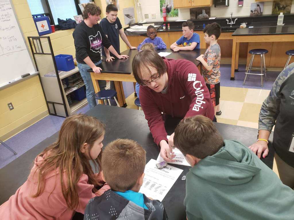 3rd grade students sitting at lab tables learning from high school students