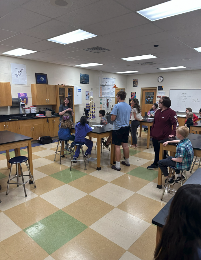 3rd grade students sitting at lab tables learning from high school students