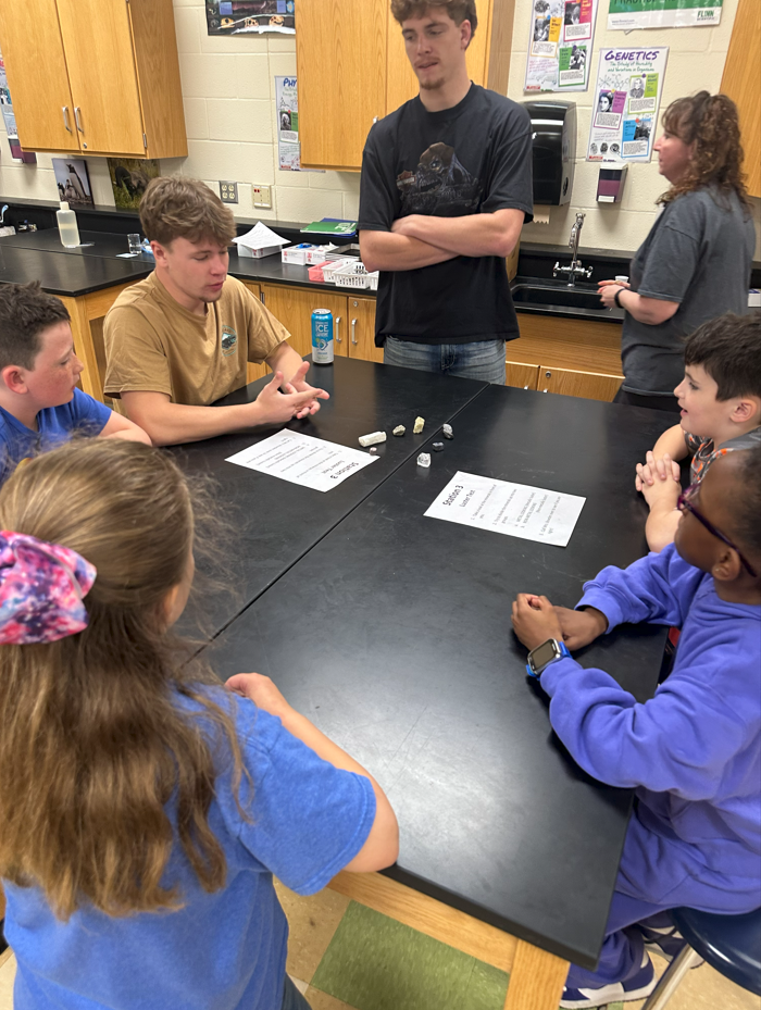 3rd grade students sitting at lab tables learning from high school students