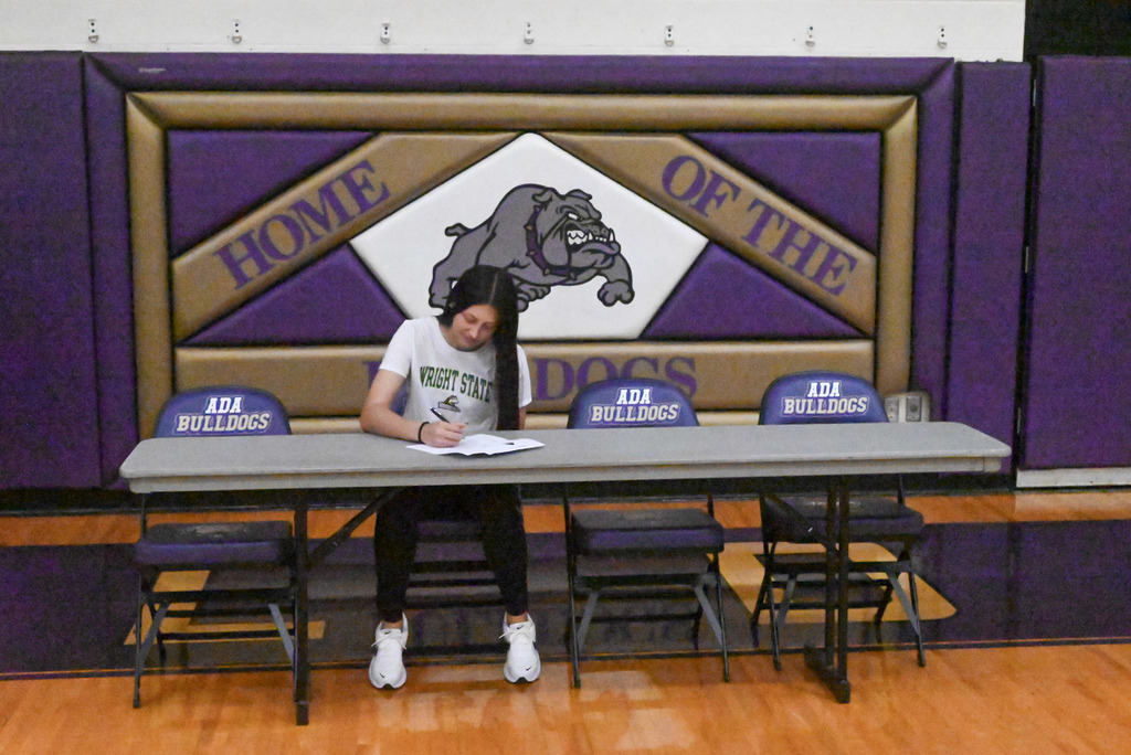 Student sitting at table with purple and gold bulldog background and college flag