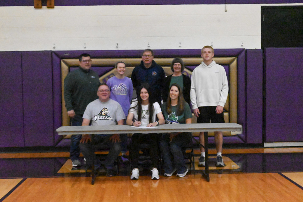 Student sitting at table with purple and gold bulldog background and college flag