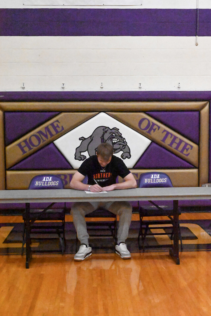 Student sitting at table with purple and gold bulldog background and college flag