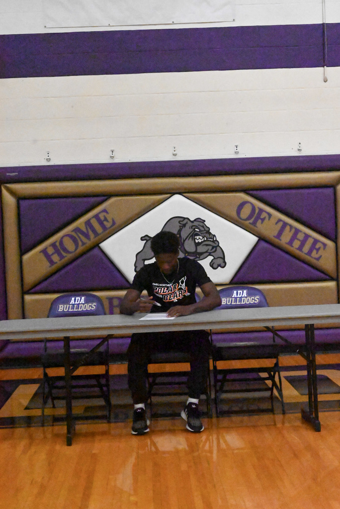 Student sitting at table with purple and gold bulldog background and college flag