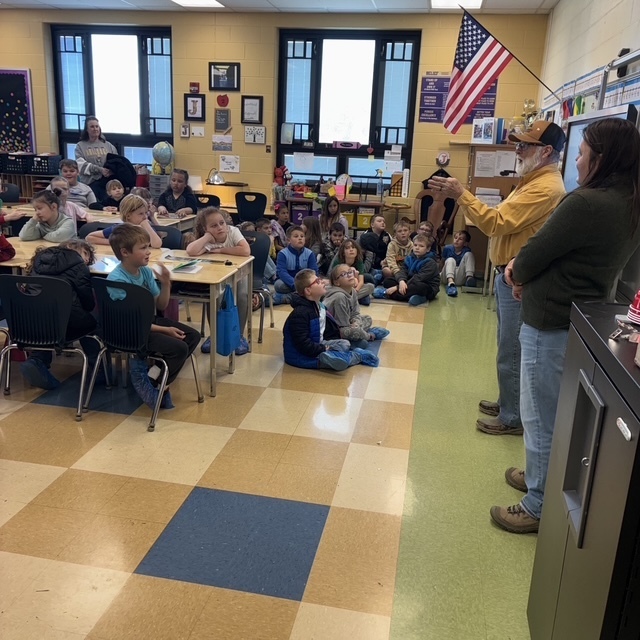 Students at desks in a classroom hearing from two adult speakers