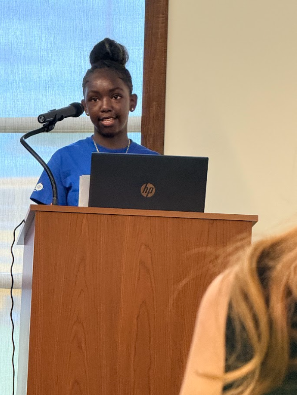 Student Speaking at podium in a blue t-shirt