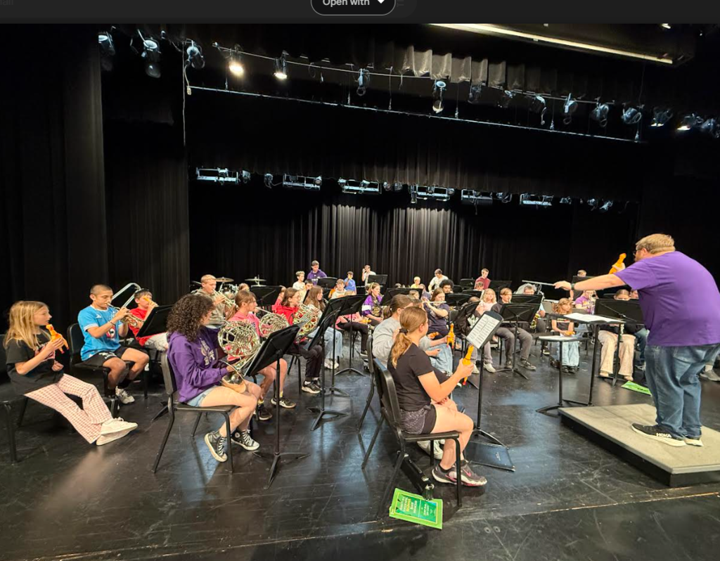 Band students sitting in chairs playing instruments on a stage