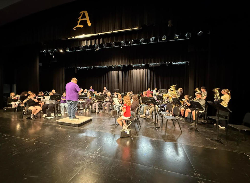 Band students sitting in chairs playing instruments on a stage